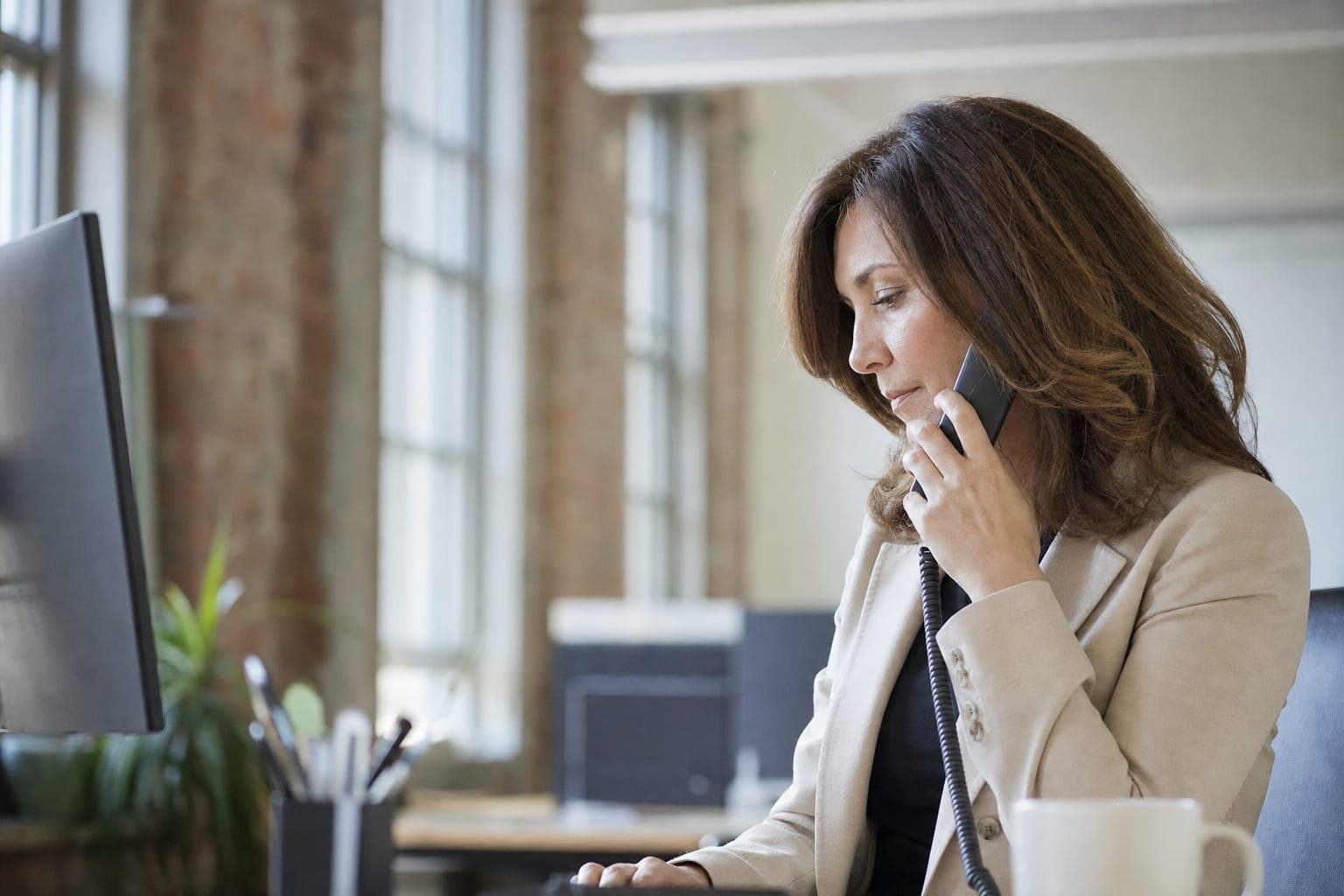 Mitarbeiterin im Telefonat am Schreibtisch, bereit für Ihr Erstgespräch